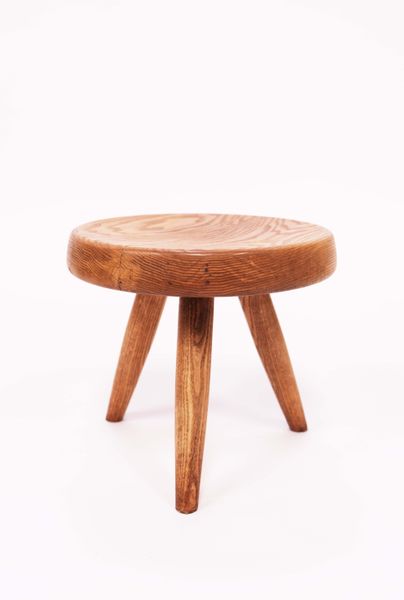 Charlotte PERRIAND (1903-1999) Tabouret dit "berger"en frêne, l'assise circulaire légèrement creusée et montée à languettes, reposant sur trois pieds fuselés. Circa 1955. H : 27,5 cm, D : 32 cm